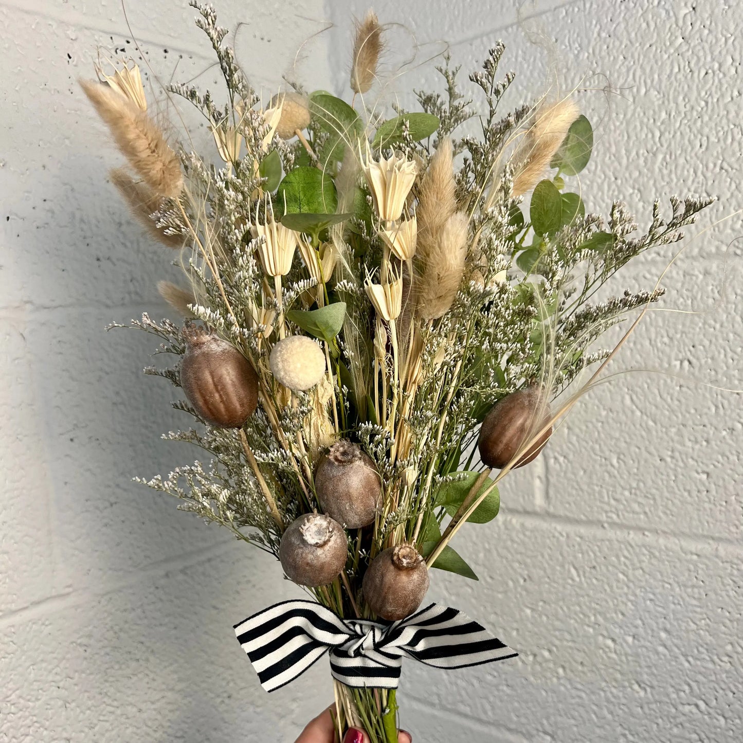 Bouquet of dried flowers with a black and white ribbon against a light gray wall.